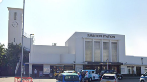 Exterior of Surbiton rail station with cars and taxis at the front.