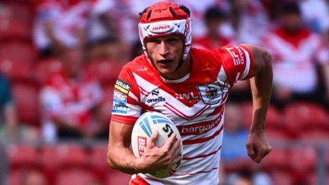 Harry Robertson, wearing St Helens' red and white jersey, runs with a rugby league ball in his right hand