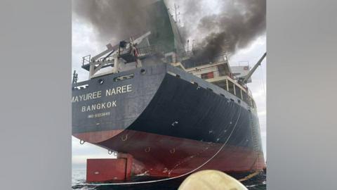Smoke seen above a cargo ship with 'Bangkok' written on it 