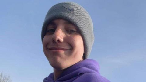 Tomasz Oleszak. He is wearing a grey beanie and a purple hoodie. He is smiling and has freckles across his cheeks.