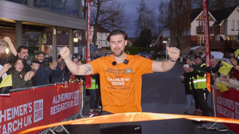 Charlie Quirke wearing an orange T-shirt crosses the finish line.