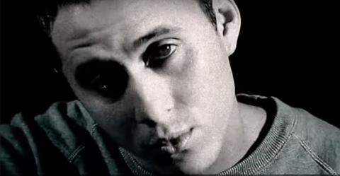 Rapper Canserbero looks at the camera in this black and white screengrab from a YouTube video. He is wearing a sweatshirt. 