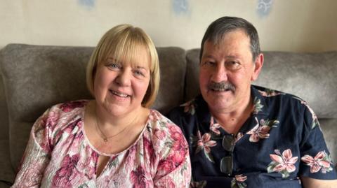 John and Catherine Canning smile at the camera from a grey sofa.