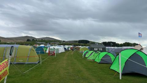 Tents pitched at Okehampton Camp. There is a view of Dartmoor in the background. 