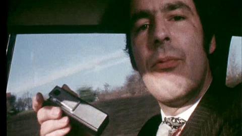 A reporter holds a beeper in a car