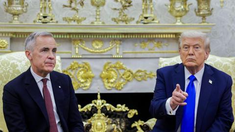 US President Donald Trump, right, and Mark Carney, Canada's prime minister, during a meeting in the Oval Office of the White House in Washington, DC, US, on Tuesday, Oct. 7, 2025. Trump is wearing a suit with a bright royal blue tie and is gesturing with his finger. Carney is wearing a suit with a burgundy tie and has a neutral expression on his face.