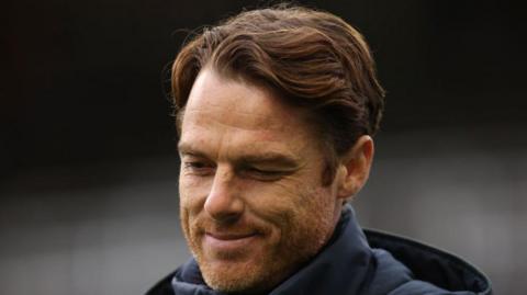 Burnley head coach Scott Parker smiling looking at the ground.