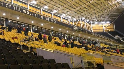 Seats in a football stadium, in blocks of yellow and black, with people sitting in some of them