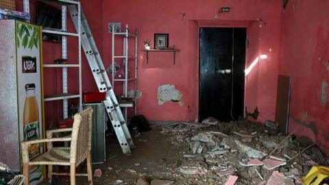 An image showing damage inside a pink house after a 6.5 magnitude earthquake in the community of San Marcos, Guerrero state, Mexico. The floor is covered in a pile broken concrete, rubble, and dirt, while a ladder is positioned on the left near shelves and a chair.