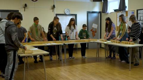 People stand around a U shaped table and play the zither