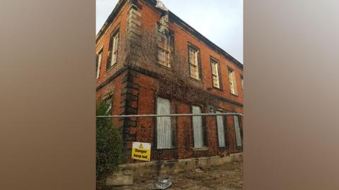 A danger keep out sign hanging n a metal fence outside an old building