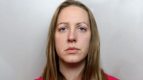 Lucy Letby, with blonde hair and a red tracksuit, sits in front of a grey background