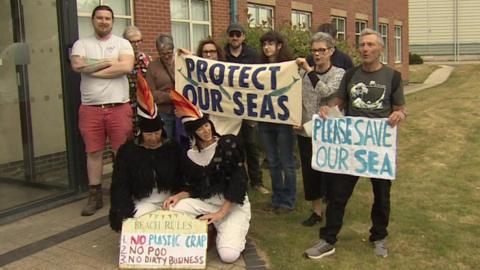 A group of campaigners outside the Port of Tyne Maritime House office, waiting to meet the firm's chief executive Matt Beeton. Two are knelt on the floor in puffin costumes. Others stand behind holding banners. One reads: "Protect our seas." Another reads: "Please save our sea." A third placcard reads: "Beach rules: No plastic crap, no poo, no dirty business."