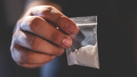 A close-up of someone's hand holding a small plastic bag containing a white powder