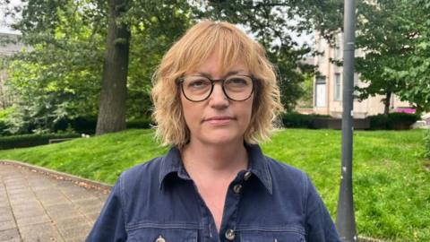 A woman with glasses standing outside looking directly into the camera 