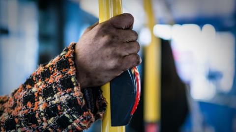 A woman's hand holds onto a rail on a bus.