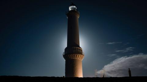 A lighthouse silhouetted against a bright moon