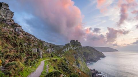 A pink hue is seen in the sky as the sun sets over a coastal path