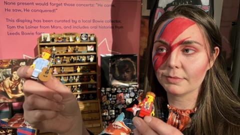 Woman with Ziggy Stardust makeup holding up David Bowie-themed Lego figurines