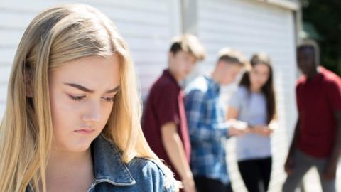 Girl standing apart from a group looking sad