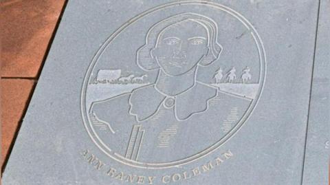 An image of Ann Raney Coleman etched on to a flagstone. The design shows a head and shoulders image of a woman with short hair. Behind her are three men on horses and a horse-drawn cart.