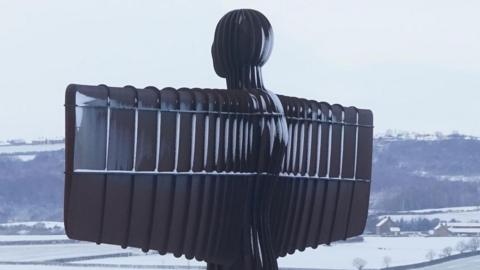 Antony Gormley's Angel of the North sculpture in Gateshead. The tall sculpture, which resembles a man with rectangular wings, is dusted with snow.
