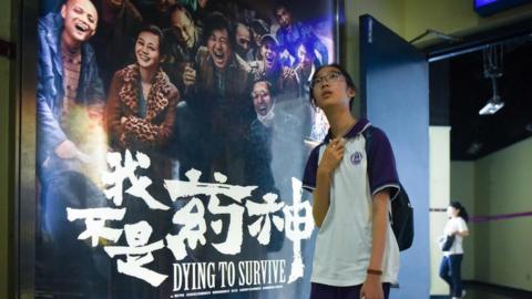 A girl walks past a poster of the film Dying to Survive at a cinema in Beijing, 12 July