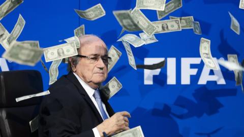 Suspended Fifa president Sepp Blatter looks on as fake dollar notes fly around him, thrown by a British comedian during a press conference