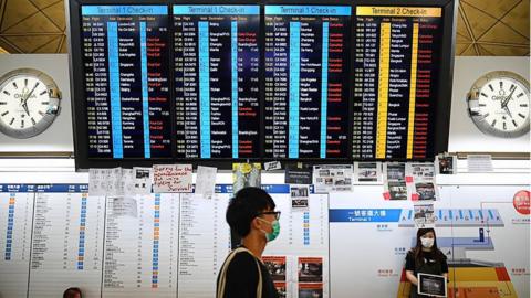 protester walks past an electronic board showing cancelled flights