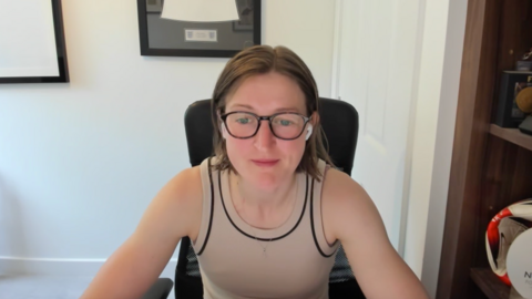 A woman with bobbed, dark hair and glasses sits in an office chair