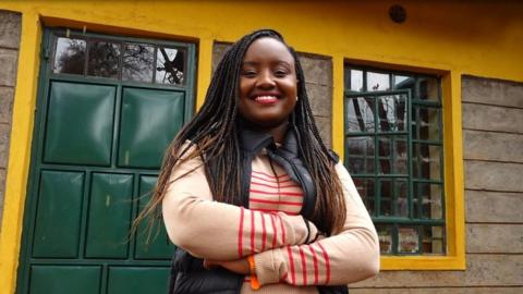 Waira Njiru smiles in front of a school building