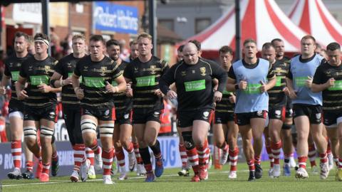 A group of Gloucester players jog past the Shed at Kingsholm during a pre-game warm-up