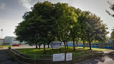 Bishopston Comprehensive School car park entrance, with trees in front of the school building and sports building