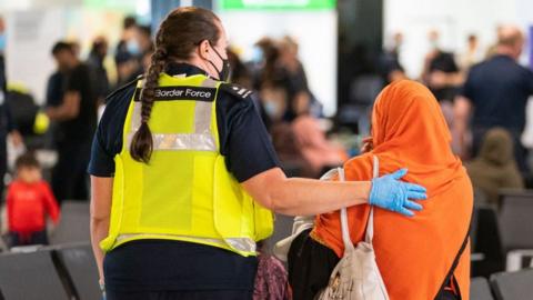 A border force official assists and Afghan refugee on her arrival to Heathrow airport