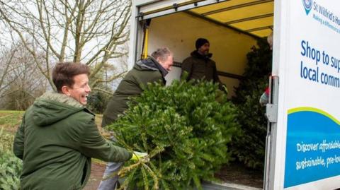Three volunteers loading Christmas trees into a van