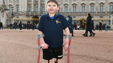 Tony Hudgell on his crutches standing posing outside Buckingham Palace