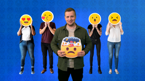 A man stands in the middle of a group of four people holding an emoji in his hand. The rest of the group have emojis for faces