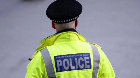 A police officer is wearing a black police hat and a high-vis jacket with the words: "Greater Manchester Police" on the back.