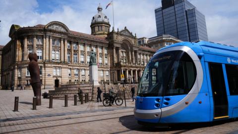 The outside of Birmingham City Council's council house, with a statue of Queen Victoria in front and a blue tram crossing in front.