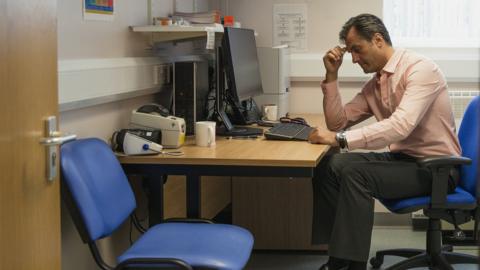 A GP sits at his desk