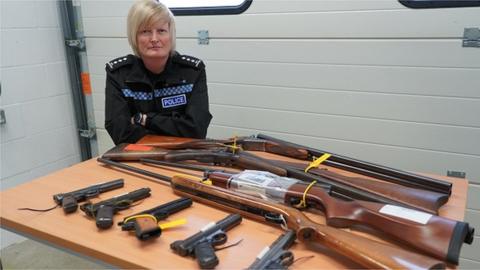 A police officer in front of table laid out with surrendered guns