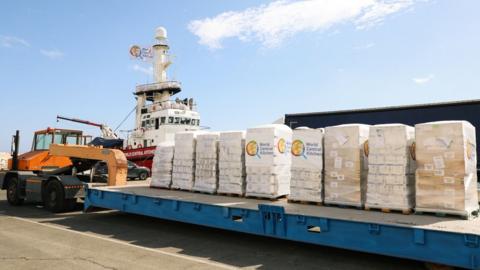 Picture of a barge with several food packages on top, in front of the aid ship Open Arms, in Larnaca, Cyprus