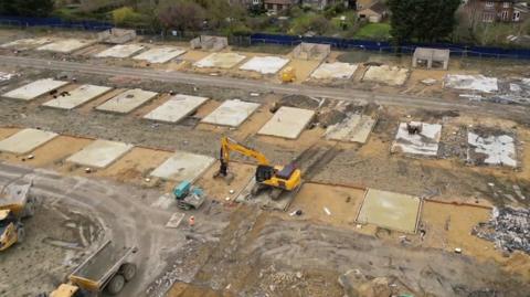 Drone footage shows a digger completing the demolition of 83 new-build homes at Darwin Green in Cambridge.