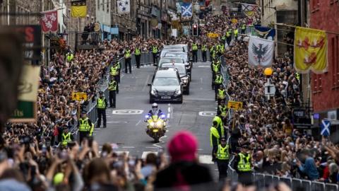 Members of the public gather on the Royal Mile in Edinburgh to watch the hearse carrying the coffin of Queen Elizabeth II passes by