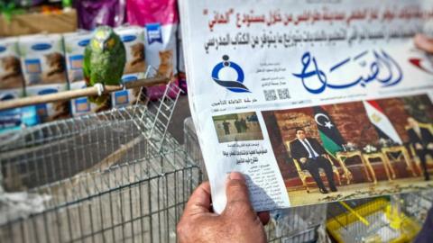 A man reads a newspaper in Tripoli with a front page article about the postponement of Libya's presidential elections, December 2021