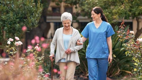 A nurse and a woman with a walking stick in an outdoor space