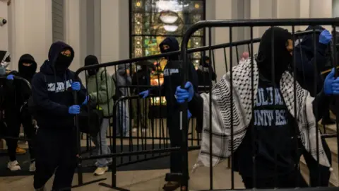 Students carrying metal barricades inside Hamilton Hall with their faces covered to hide their identity