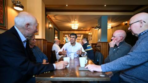 Rishi Sunak sits at a table and meets with veterans