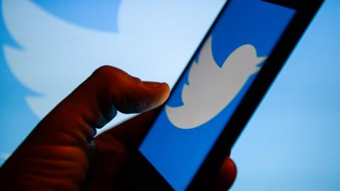 Stock image of a man using a phone, with the screen showing the twitter logo