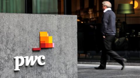 The PricewaterhouseCoopers (PwC) logo with businessman walking, in front of the PwC offices in More London Riverside